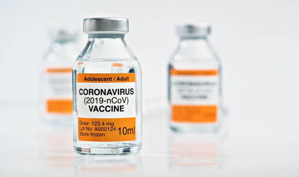 istock Coronavirus Covid 19 vaccine concept - small glass vials with silver caps on white table, closeup detail (own sticker design with dummy data - not real product) 1255172260