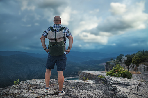 Confident man stands alone on top of the mountain against overcast sky