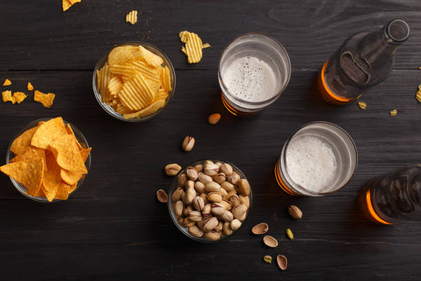 birra in bottiglie e bicchieri, patatine, nachos e pistacchi in piatti di vetro e sparsi - beer nuts foto e immagini stock