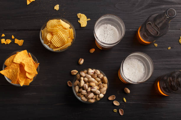 beer in bottles and glasses, chips, nachos and pistachios in glass plates and scattered - beer nuts imagens e fotografias de stock