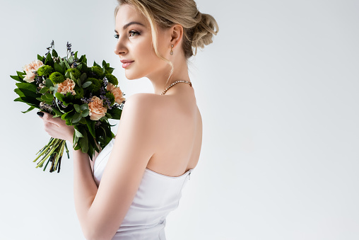 attractive bride in wedding dress holding flowers on white