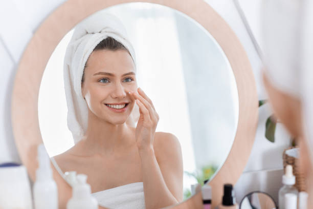 istock Happy young woman using face cream after shower 1255175343