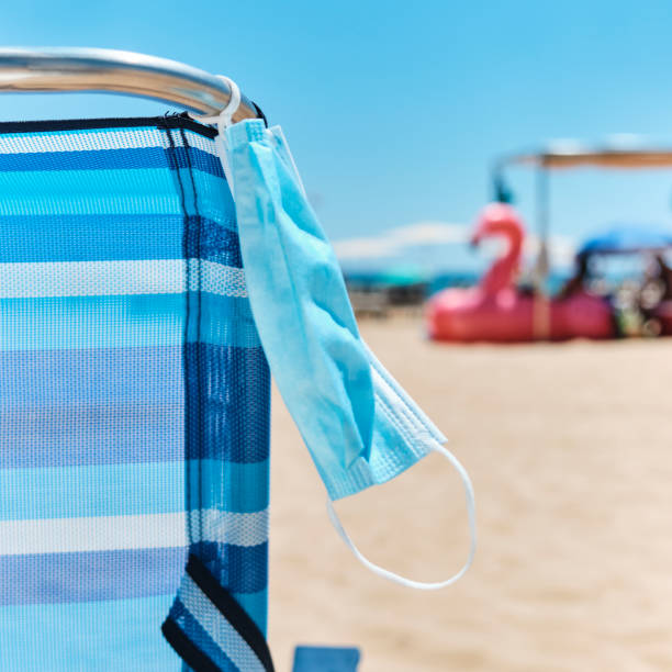 istock surgical mask hanging on a deck chair on the beach 1255175445