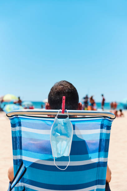 istock mask and man sitting in a deck chair on the beach 1255175487