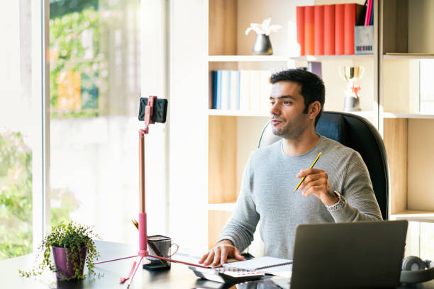 istock A young businessman sitting and working at home on a desk with a mobile phone and a notebook computer And meeting through the application. 1255176641