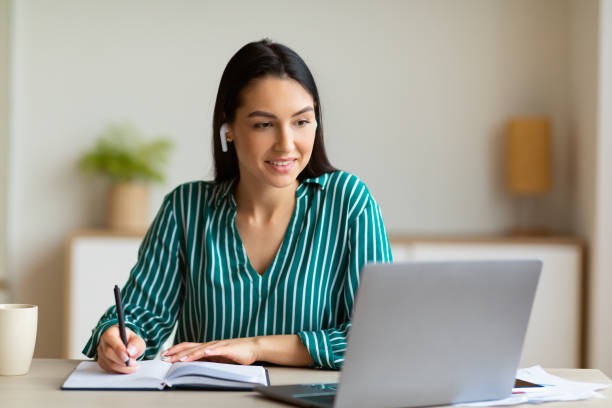 istock Woman At Laptop Taking Notes Learning Wearing Earbuds In Office 1255176878