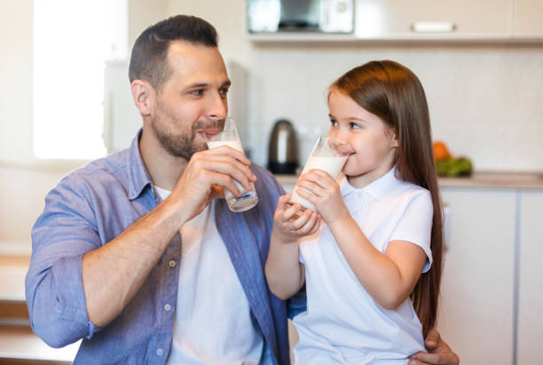 father and little daughter drinking milk in kitchen at home - milk child drinking little girls imagens e fotografias de stock