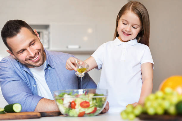 istock Smiling Father And Daughter Making Salad Cooking In Kitchen Indoors 1255178493