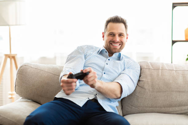 istock Young man sitting on couch playing video games 1255179027