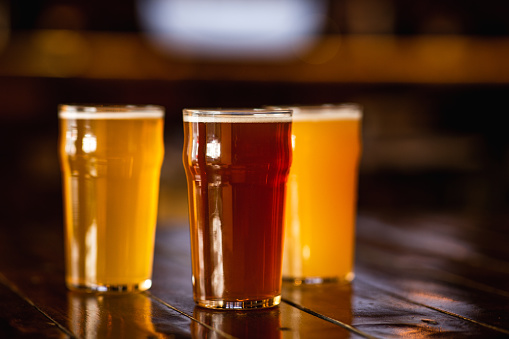 Beer craft style. Barley, unfiltered, light drink in glasses on wooden table in blurry interior of pub