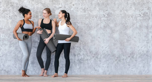klasa pilates. sportowe młode dziewczyny stojące z matami do jogi w pobliżu szarej ściany - yoga class caucasian young adult group of people zdjęcia i obrazy z banku zdjęć