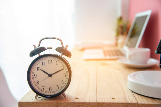 istock Alarm clock on work tale deadline time business concept. Alarm awake reminder appointment time agenda. selective focus clock on wooden table with coffee cup and laptop with soft sunlight. 1255183329