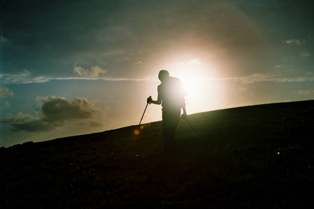 istock Female Hiker Silhouette on an open field with the sun setting 1255186436