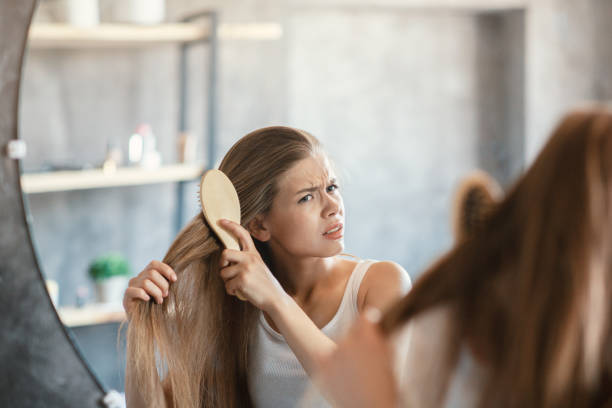 Frustrated young woman trying to brush her tangled hair in front of mirror in bathroom Frustrated young woman trying to brush her tangled hair in front of mirror at bathroom frizzy stock pictures, royalty-free photos & images