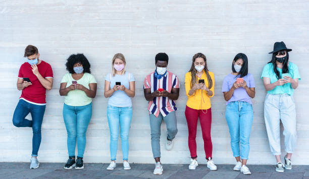 istock Young people wearing face safety masks using smart mobile phones while keeping social distance during coronavirus time - Technology and covid-19 spread prevention concept - Main focus on center faces 1255190447