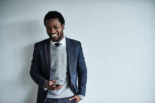 Portrait of a handsome young businessman using a cellphone against a grey background