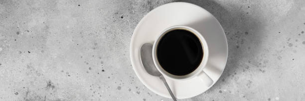 istock Banner. A white Cup of coffee on a gray table. Top view with space for text 1255191199