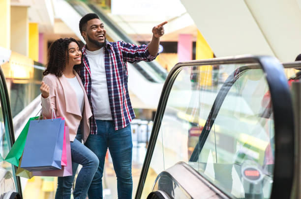 istock Black millennial couple going up the escalator in mall and pointing aside 1255191348