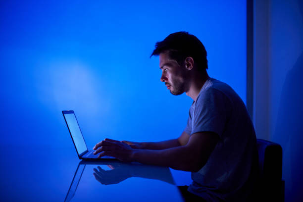 hacker mencoba memecahkan sistem keamanan untuk mencuri informasi perusahaan penting, bekerja di laptop dalam cahaya neon biru - agen judi online potret stok, foto, & gambar bebas royalti