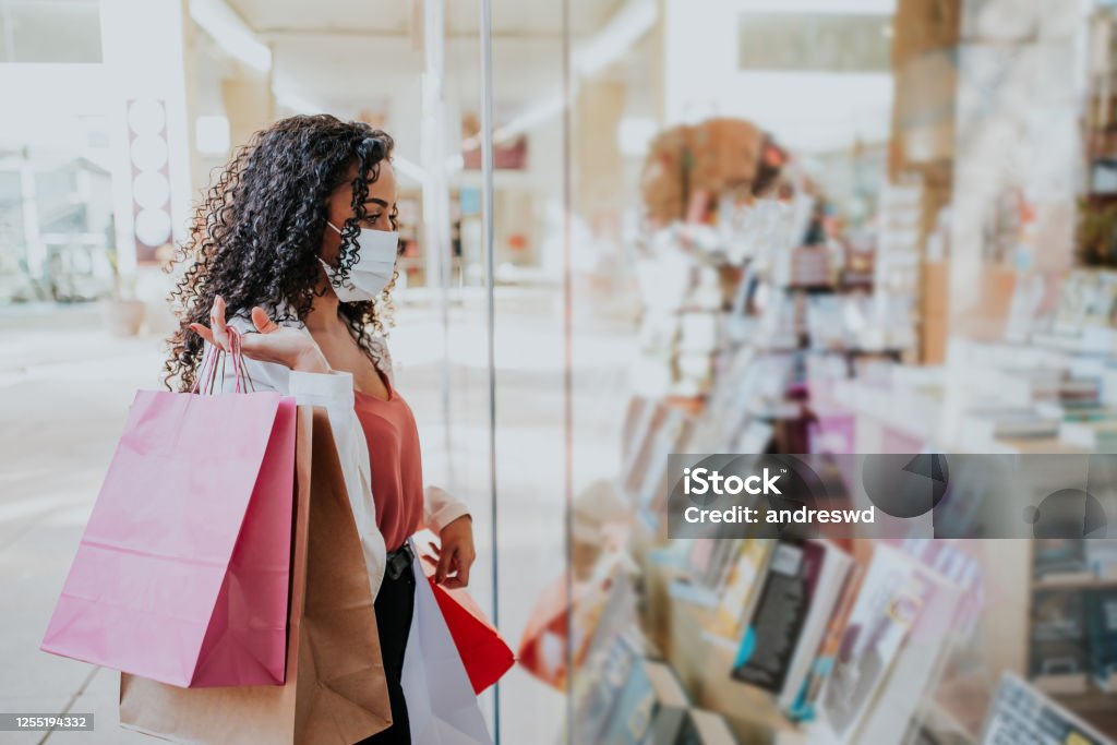Woman in shopping mall with bags shopping Woman in shopping mall with bags shopping during pandemic and wearing face mask against coronavirus Retail Stock Photo