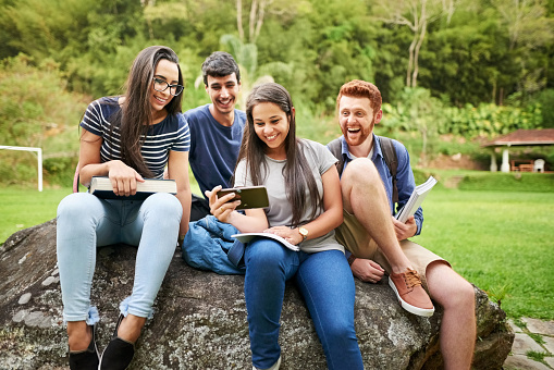 Group of students sitting together in campus looking at a mobile phone and smiling
