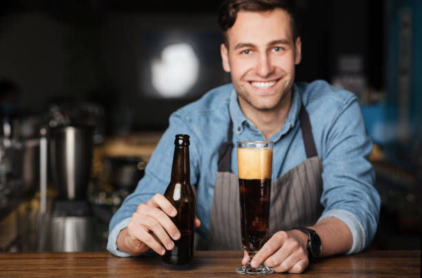 istock Fresh beer for client. Smiling bartender pours dark drink in high glass 1255196309