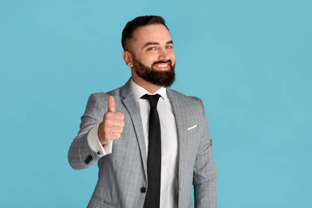 istock Cheerful millennial businessman showing thumb up gesture on blue background 1255196836