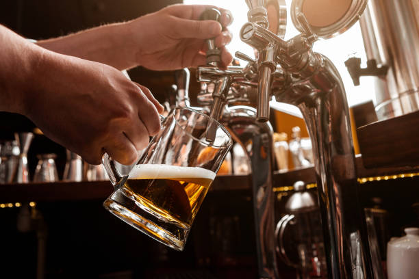 istock Work bartender. Bartender pours beer from tap in glass mug in interior of pub 1255197656