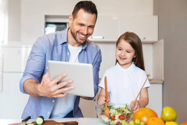 istock Cheerful Dad And Daughter Cooking Using Digital Tablet In Kitchen 1255198118