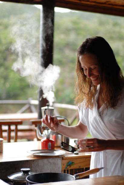 Beautiful Woman cooking with coffee pot steaming behind her at a cabin on a open air porch