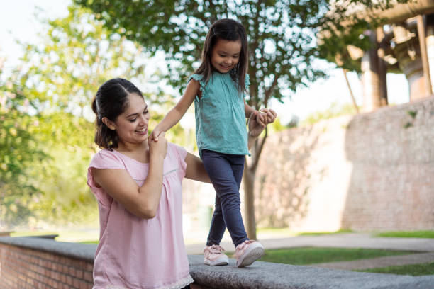 Young mother holding daughter walking on low wall stock photo