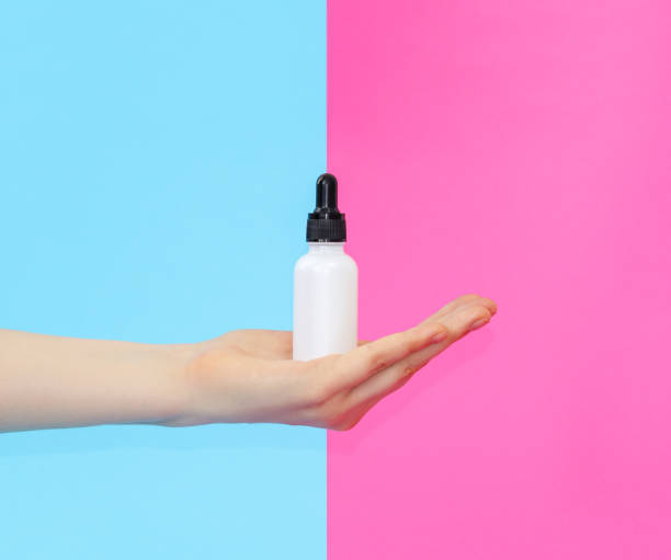 istock Collagen serum in a white light bottle on blue-pink. Bottle in hand. 1255202233