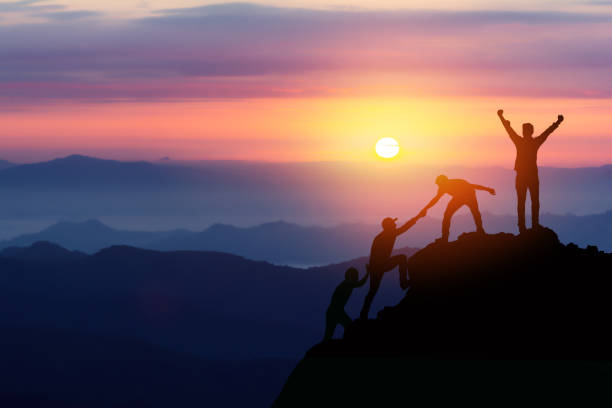 チームワークの友情ハイキングは、山、日の出でお互いに信頼支援シルエットを助けます。登山チームの美しい日の出の風景の上でお互いを助け合う2人の男性ハイカーのチームワーク - アジア大陸 写真 ストックフォトと画像