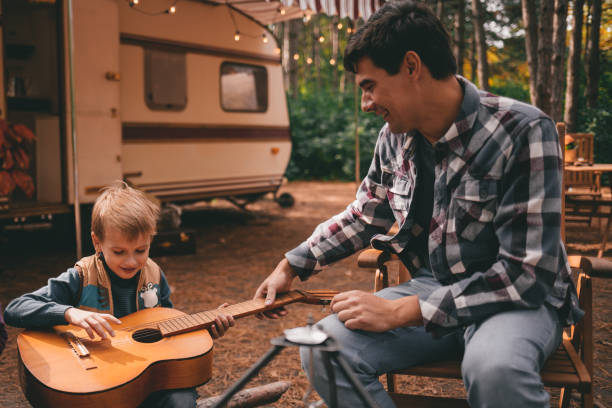 Father teaches son play guitar on camping trip relaxing in the autumn forest. Camper trailer. Fall season outdoors trip Father teaches son play guitar on camping trip relaxing in the autumn forest. Camper trailer. Fall season outdoors trip motor home photos stock pictures, royalty-free photos & images