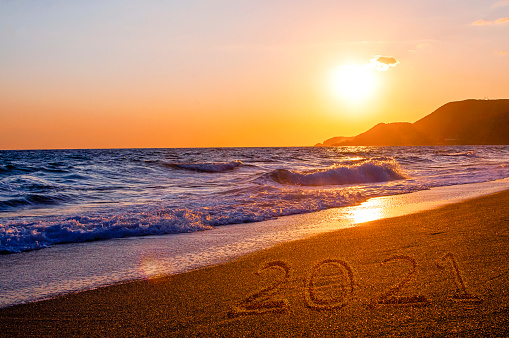New year 2021 written on sandy beach with waves