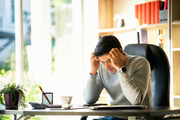 istock A young businessman sitting and working at home on a desk with a mobile phone and a notebook computer And Young men are stressed at work. 1255207039