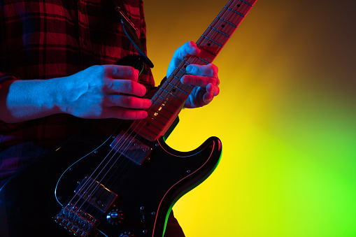 Close up young inspired and expressive musician, guitarist performing on gradient colored background in neon light. Concept of music, hobby, festival, art. Joyful artist, colorful, bright portrait.