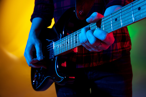 Close up young inspired and expressive musician, guitarist performing on gradient colored background in neon light. Concept of music, hobby, festival, art. Joyful artist, colorful, bright portrait.