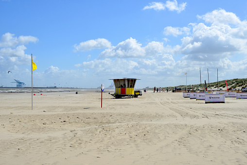 Blankenberge, Belgium - June 28, 2020: beach life. Yellow flag for swimming alert. Background Zeebrugge port. Social distancing white screens per family sun bathing compartmentalization.