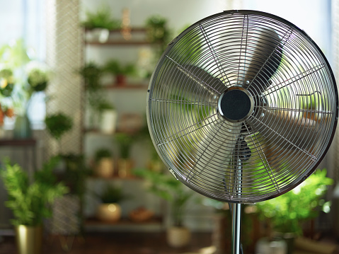 Summer heat. modern metallic floor stand electric fan at modern home in sunny hot summer day.