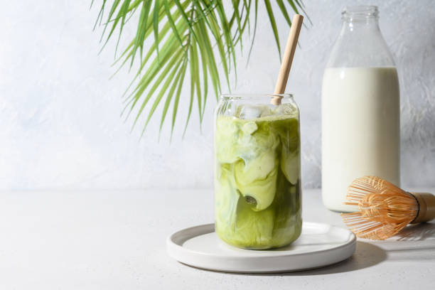 thé de matcha vert glacé mélangé avec le cube de glace et le lait dans le verre de latte sur le blanc. - latté photos et images de collection