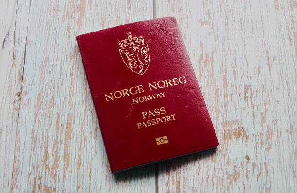 business travel Norwegian passport on a light blue wooden background with a computer in a business travel setting. Norwegian passport cover. Norwegian Passports are issued to nationals of Norway for the purpose of international travel. The passport may also serve as proof of Norwegian citizenship and is valid for ten years. The passport shares the standardised layout of most European Union countries, as Norway has implemented the EU passport regulation. norwegian culture photos stock pictures, royalty-free photos & images
