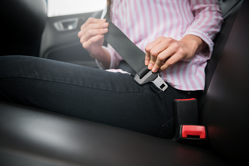 Close-up on a female passenger fastening her seat belt in a car - lifestyle concepts