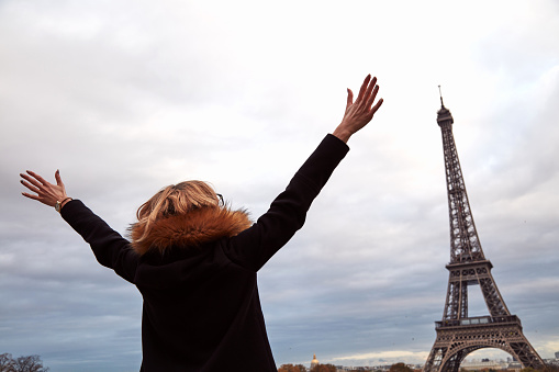 Woman with arms wide open in front of a Eiffel tower, Paris, France.