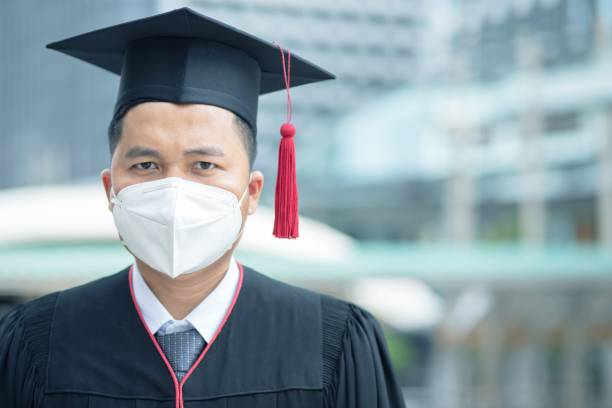 The Graduate is wearing a mask to protect the Corona virus from the university. The Graduate is wearing a mask to protect the Corona virus from the university. ritual mask stock pictures, royalty-free photos & images