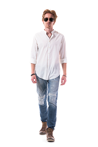 Fashionable young man in jeans walking and looking approaching to camera. Full body length isolated on white background.