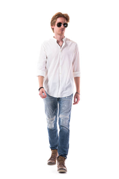stylish fashionable young modern man in jeans walking approaching and looking away - arms at side imagens e fotografias de stock