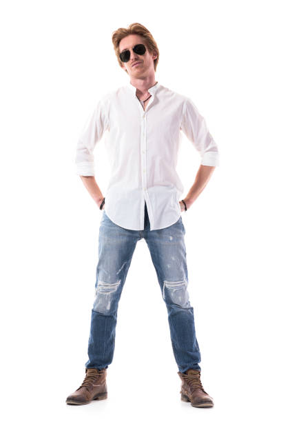 istock Happy handsome young man in white shirt and jeans posing with hands in back pockets 1255243187