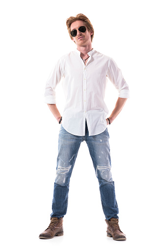 Happy handsome young man in white shirt and jeans posing with hands in back pockets. Full body length isolated on white background.