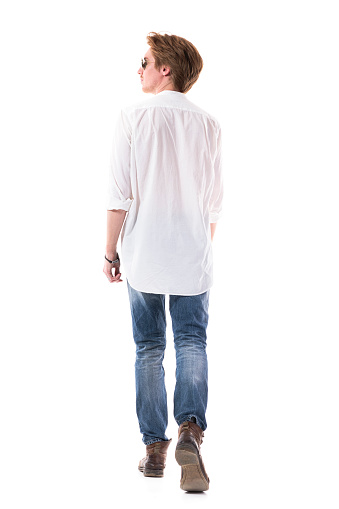 Back view of handsome elegant young man in jeans walking away looking up. Full body length isolated on white background.